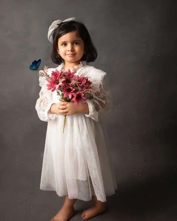 A timeless portrait in a beautiful white lace dress against a classic mottled grey backdrop. The added butterfly gives it a touch of magic.