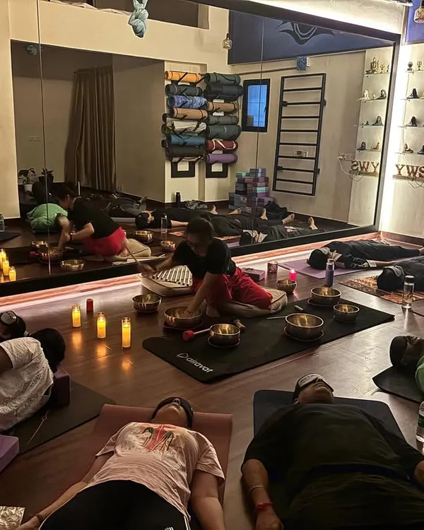 A wide view of a group sound bath, showing participants in a state of deep rest. The room is filled with the warm glow of candles, creating a perfect environment for healing and letting go.