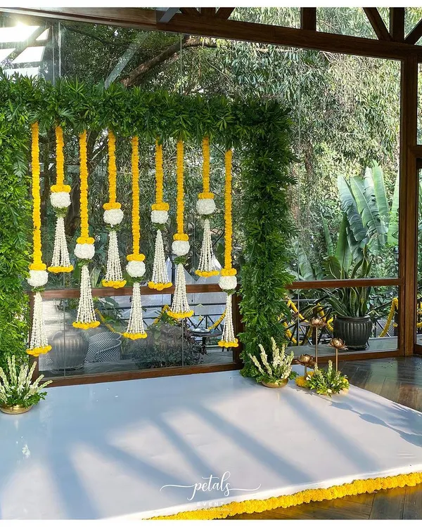For this indoor engagement, I created a stunning backdrop with a lush frame of ferns. Hanging floral streamers of marigolds and tuberoses add a traditional touch to the modern, natural setting.