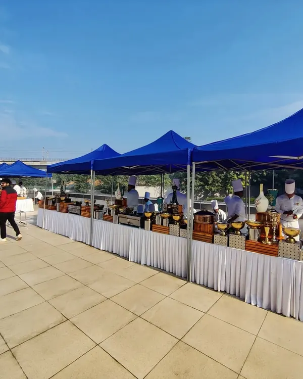 This is the catering setup for an Indigo Airlines corporate event. We provided a long line of buffet stations under protective blue canopies, ensuring a professional and organized food service area for the guests.