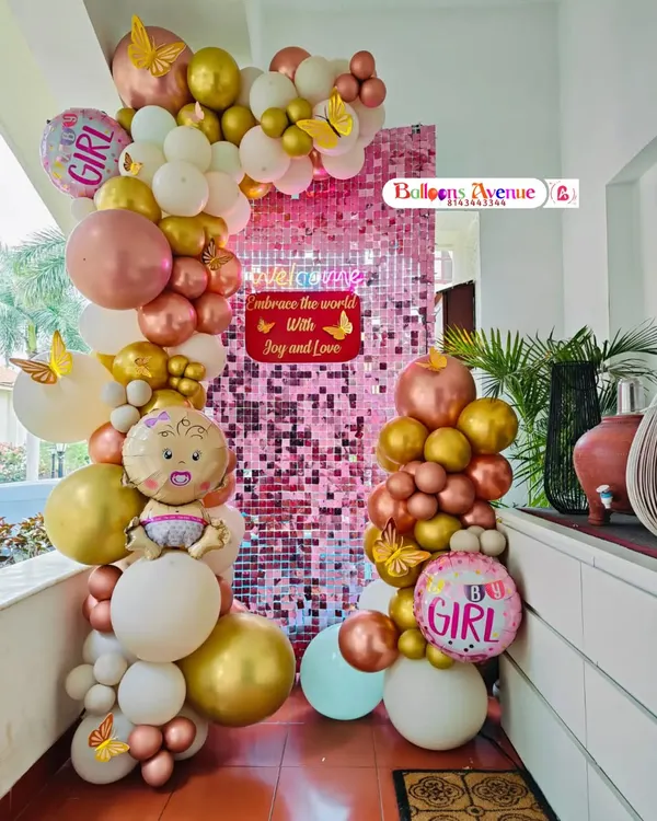 A full view of the pink shimmer wall setup for a baby girl celebration, complete with "It's a Girl" foil balloons.