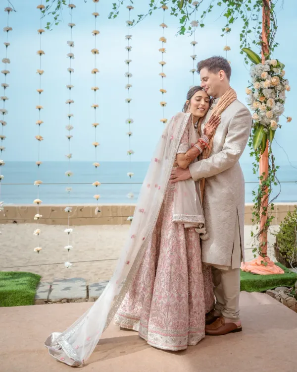 A romantic portrait of a couple embracing on their wedding day, with a beautiful backdrop of the ocean and a floral arch.