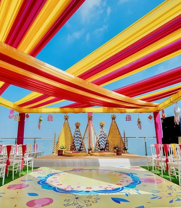 A vibrant Haldi ceremony set against a stunning seaside backdrop. We used bright yellow and pink fabric drapes to create a festive canopy, with a custom-printed floor and floral arrangements that make for incredible photos and an even better experience.