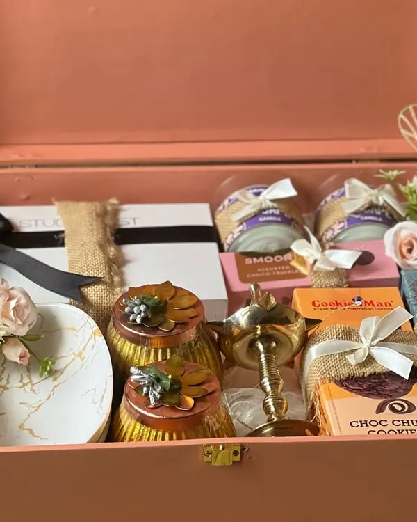 This premium hamper, presented in a beautiful peach-colored trunk, is curated with luxury items for a truly special gift. It includes scented candles, artisanal cookies, decorative diyas, and men's grooming products, making it a perfect engagement or wedding present.