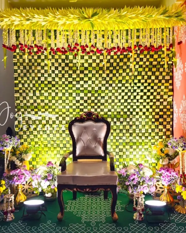 An elaborate and traditional decoration for a half saree ceremony. This setup features a woven banana leaf backdrop, a canopy of jasmine and rose petals, and a beautiful kolam design on the floor.