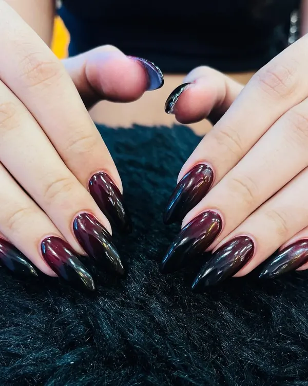 A dark and dramatic ombre effect. These long, almond-shaped nails transition from a deep burgundy at the base to a solid black at the tip, creating a moody and sophisticated look.