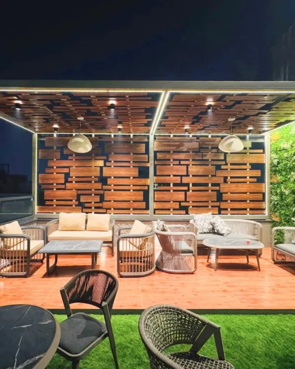 A closer look at our rooftop lounge design, focusing on the main seating area. The combination of a wooden deck, a vertical green wall, and a slatted wood feature wall creates a rich, textured environment. The comfortable sofas and ambient pendant lights make it an inviting space for evening conversations.