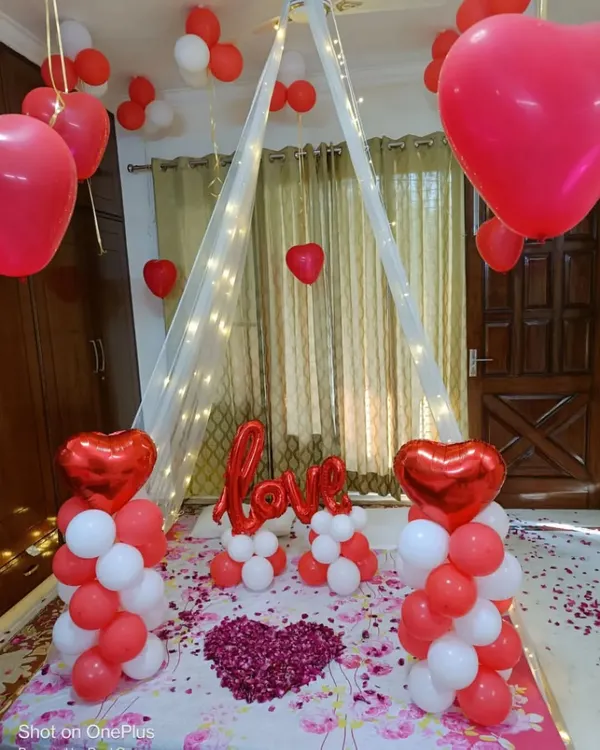 A classic red and white romantic room decoration. I created a beautiful canopy with fairy lights over the bed, flanked by balloon pillars and a "LOVE" message, with a heart made of rose petals as the centerpiece.