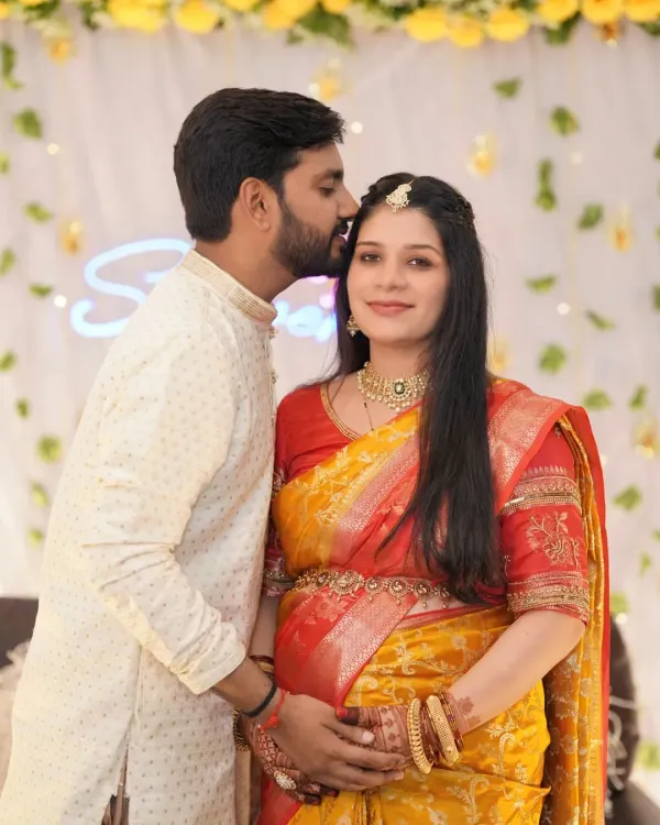 A tender moment from a baby shower celebration. The father-to-be kisses his wife's forehead as she smiles, capturing the love and excitement of the day.