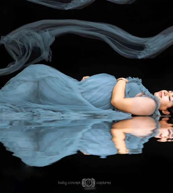 An artistic fine art portrait showing an expecting mother in a dusty blue gown, lying on a reflective surface. The composition creates a stunning mirror image, highlighting the serene beauty of pregnancy.