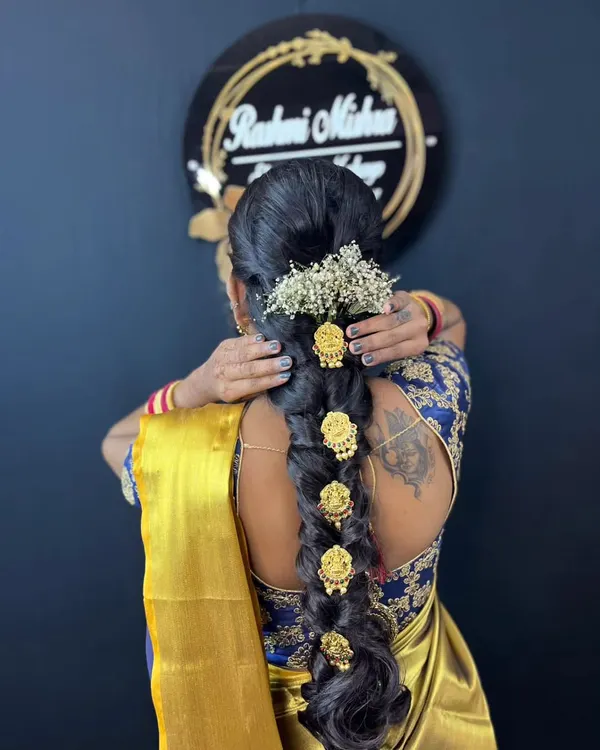A detailed view of a traditional South Indian bridal hairstyle, featuring a long braid decorated with intricate gold accessories and fresh baby's breath flowers.