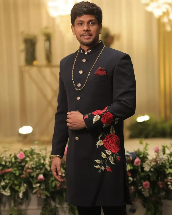 A masterpiece of traditional tailoring. This client is wearing a custom navy blue sherwani featuring stunning red rose embroidery, a design we created to symbolize a sibling bond for a wedding.