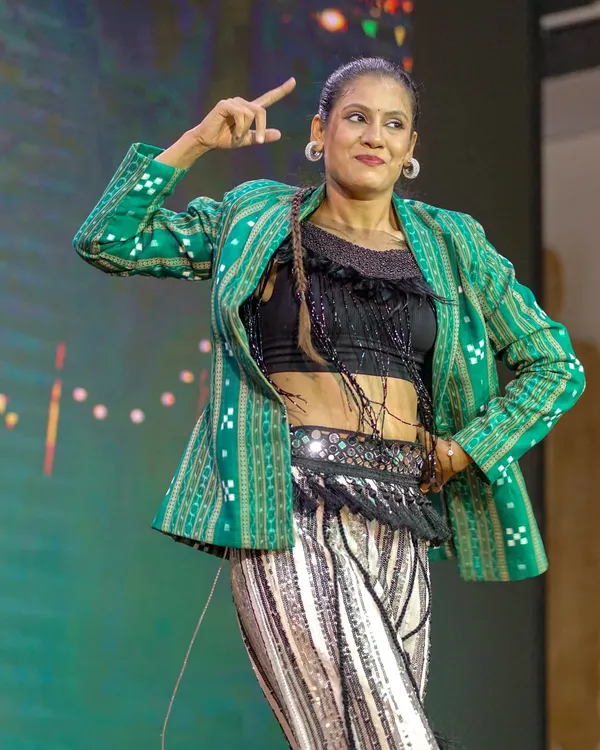 A dynamic pose during a performance that fuses modern dance with Odia cultural elements. The green Sambalpuri jacket adds an authentic touch to the contemporary outfit.