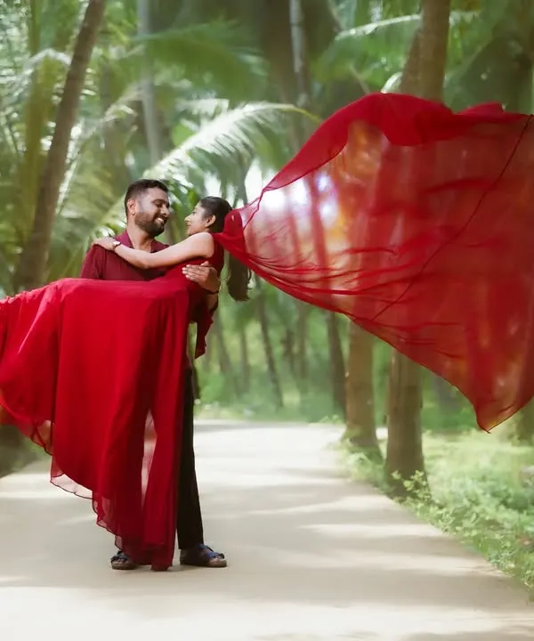 A classic romantic pre-wedding pose with the groom lifting the bride, her vibrant red gown flowing in the wind. This shot, set against a backdrop of palm trees, is perfect for creating a dramatic and memorable image.