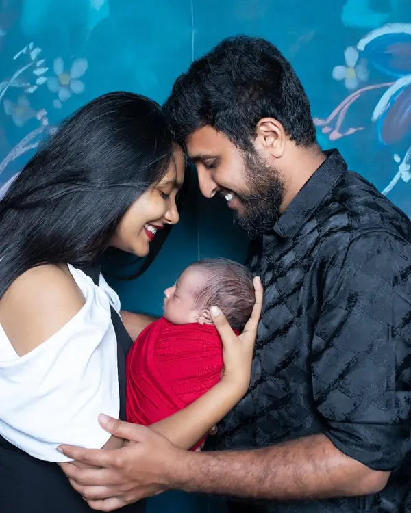 New parents share a happy, intimate moment, their foreheads touching as they cradle their newborn wrapped in a bright red swaddle.