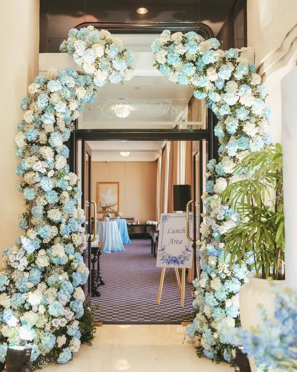 A breathtaking floral arch in shades of blue and white creates a grand yet welcoming entrance. The dense hydrangeas and roses set a luxurious and romantic tone from the moment guests arrive.