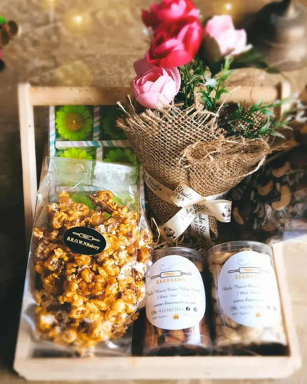 Our Floral Indulgence Gourmet Hamper is curated to delight all senses. It includes caramel popcorn, jars of roasted nuts, handcrafted chocolates, and a rustic mini bouquet, all arranged in a charming wooden crate.