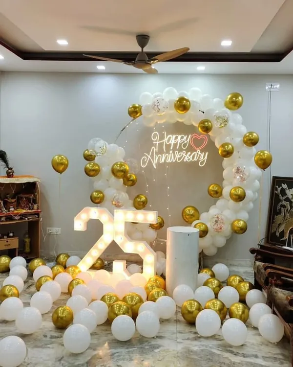 This elegant 25th-anniversary decoration in a home setting shows a complete package. It includes a white and gold balloon ring, a "Happy Anniversary" neon sign for a warm glow, and large light-up "25" numbers that serve as a fantastic centerpiece.