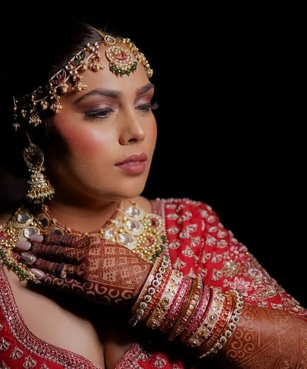A stunning bridal portrait against a black background. The bride's intricate jewelry, henna, and confident pose are highlighted beautifully.