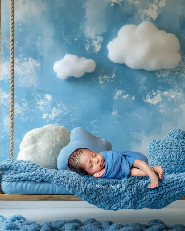 A newborn rests peacefully on a dreamy swing set against a sky-blue backdrop, showcasing our creative and artistic approach to newborn photography. We design unique, safe, and beautiful sets like this in our Bangalore studio.