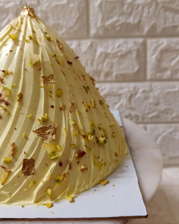 A close-up of my special Modak Cake, created for Ganesh Chaturthi. It’s a vanilla cake filled with coconut-jaggery saran, frosted beautifully, and garnished with pistachios and gold leaf.