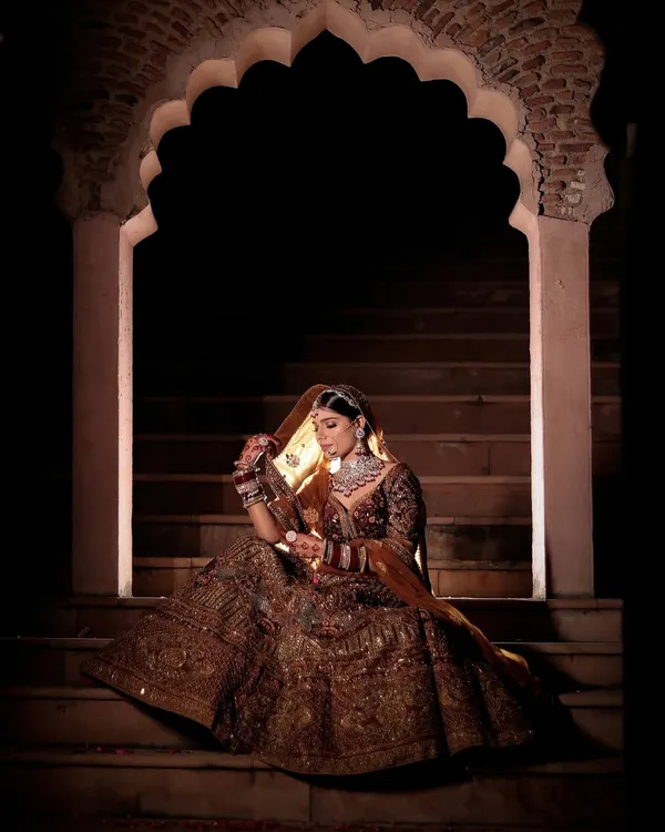 This is the kind of dramatic, royal shot we love to create. Using bold lighting and shadows against a heritage backdrop, we capture a portrait that feels both timeless and powerful, focusing on the bride's magnificent lehenga and solitary grace.