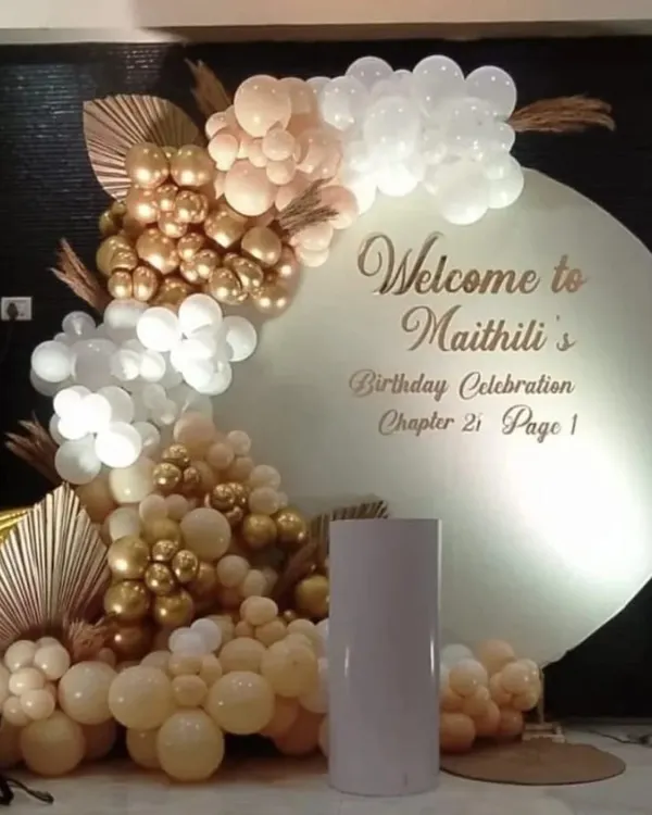 A sophisticated welcome backdrop for a 21st birthday. This setup features a personalized circular board and an organic balloon garland in a chic palette of white, beige, and chrome gold.