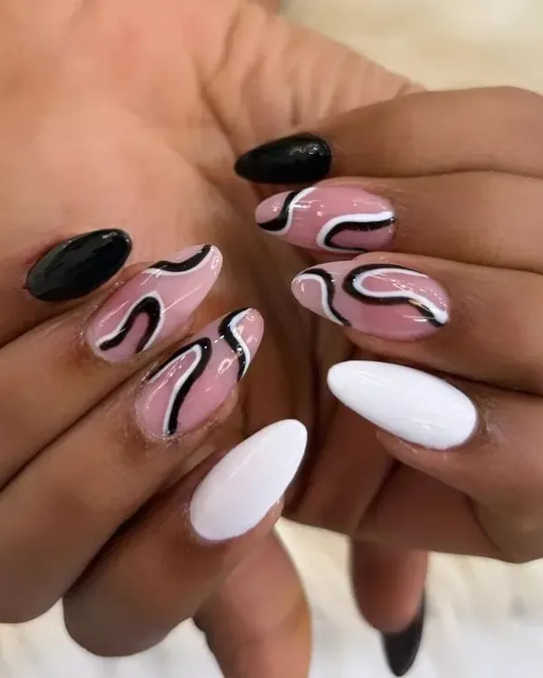 A trendy and artistic manicure featuring abstract designs. This set combines solid black and white nails with accent nails that have a nude base and bold, free-flowing black and white swirls.
