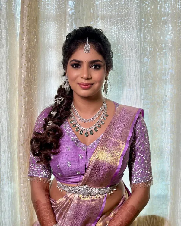 A beautiful engagement look for Charu. The makeup features a soft smokey eye and a neutral lip, paired with a modern braided hairstyle and a lovely lavender saree.
