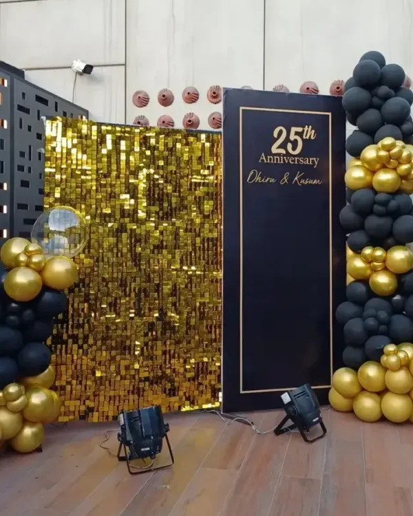 A sophisticated black and gold backdrop for a 25th anniversary party. This setup features a gold sequin panel, a personalized sign, and dramatic balloon garlands, all highlighted with professional spotlights.