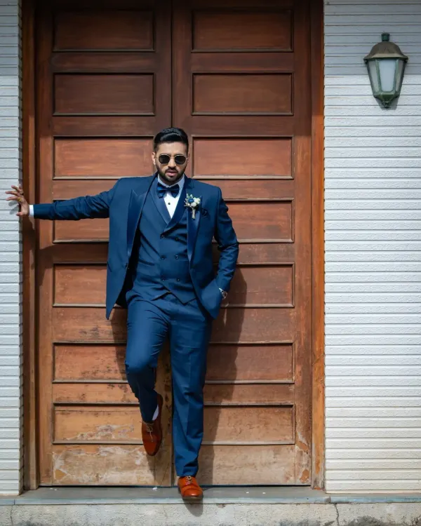 A groom with style. This portrait captures a cool, confident look as he leans against a rustic wooden door, ready for the big day.