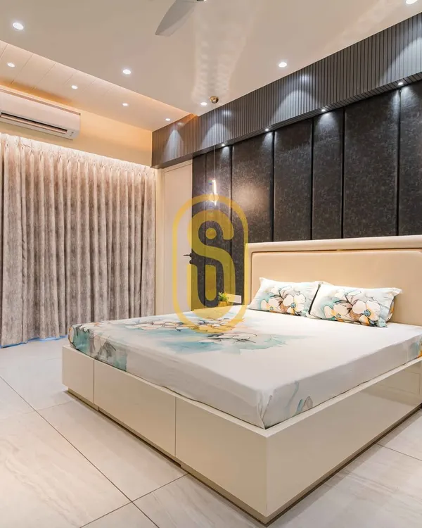 A bright and airy bedroom featuring a dark grey upholstered accent wall with integrated lighting. The custom bed includes built-in storage drawers, demonstrating our focus on functional design.