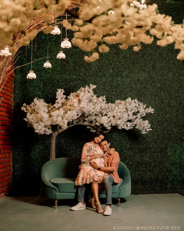 A wide shot from a styled maternity session, showing the couple seated under a canopy of lights and blossoms. This demonstrates a more creative and decorative approach to maternity photography.