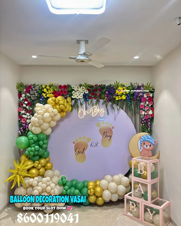 This "Oh Baby" gender reveal backdrop combines a lush floral border with a playful balloon arch in green, gold, and white. The custom backdrop with tiny footprints adds a personal and exciting touch to the celebration.