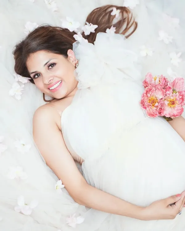 A dreamy top-down shot creating an ethereal feel. The mother-to-be is surrounded by soft white fabric and flowers, resulting in a peaceful and artistic maternity photograph.