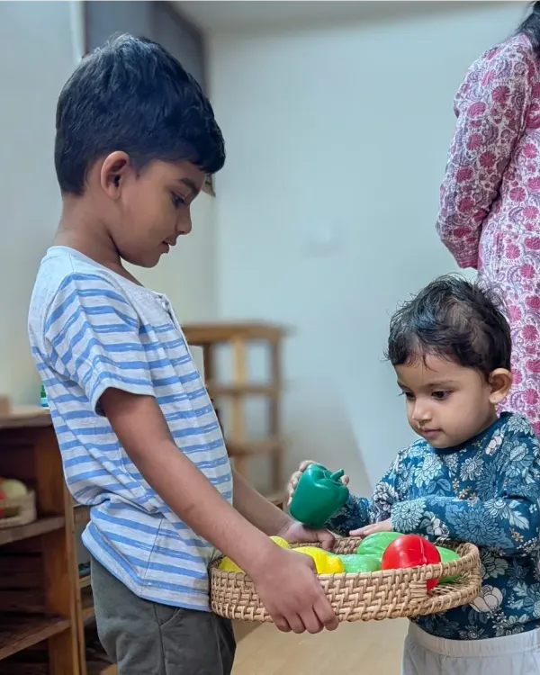 This heartwarming moment shows an older sibling, a Hastam alumnus, helping his younger sister with a basket of play vegetables on her first day. It is a perfect example of the caring and supportive peer relationships that flourish in our school.