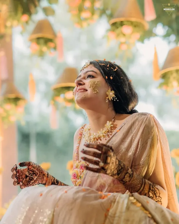A moment of pure bliss during the Haldi ceremony. The bride, adorned with turmeric and flower petals, looks up with a joyful smile, perfectly capturing the spirit of the celebration.
