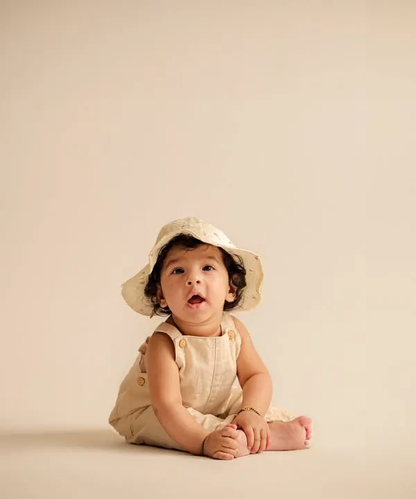 A perfect sitter session portrait. At six months, babies can often sit up unassisted, and we capture their proud smiles with simple props like this cute hat.