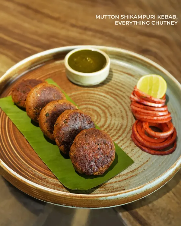 Our Mutton Shikampuri Kebabs are tender, flavorful patties served on a banana leaf. They come with our "everything chutney" and pickled onions, offering a perfect balance of spice and tang in every bite.