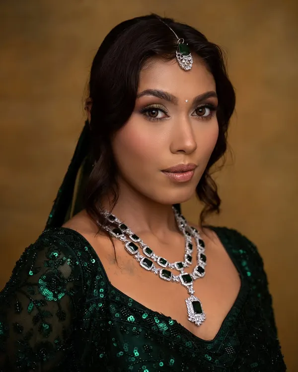 A regal and elegant look featuring a shimmery green and gold eye makeup. This look was designed to complement the emerald green lehenga and diamond jewelry, perfect for a bride's reception or sangeet.