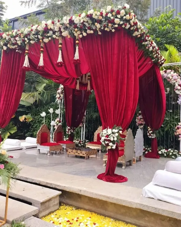 This outdoor mandap is a vision in red. We used luxurious velvet drapes, floral tassels, and a crystal chandelier to create a royal setting against a lush green backdrop, perfect for a classic Indian wedding ceremony.