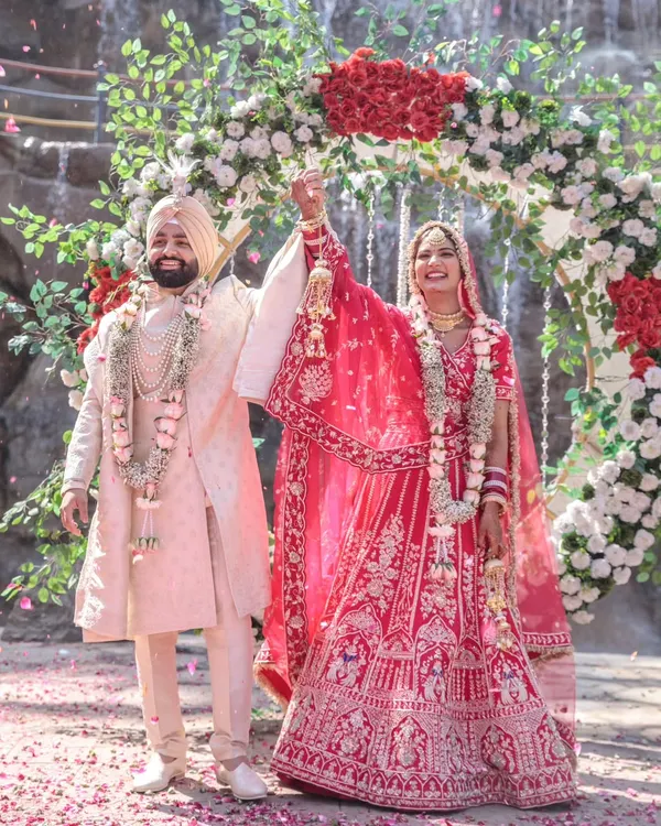 A triumphant and joyous moment as the bride and groom raise their hands after the Varmala ceremony, standing before a magnificent waterfall and floral arch.