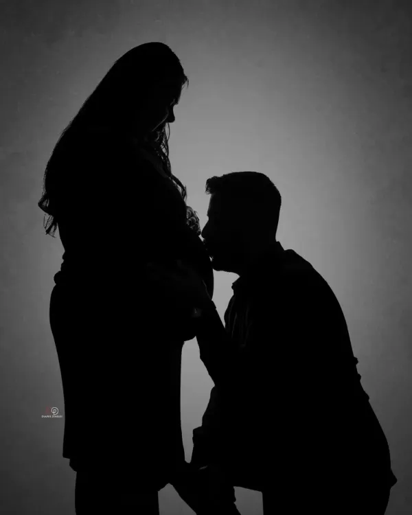 A beautiful and intimate silhouette portrait of a couple. The dad-to-be kissing the baby bump is a classic, tender moment that looks stunning in black and white.