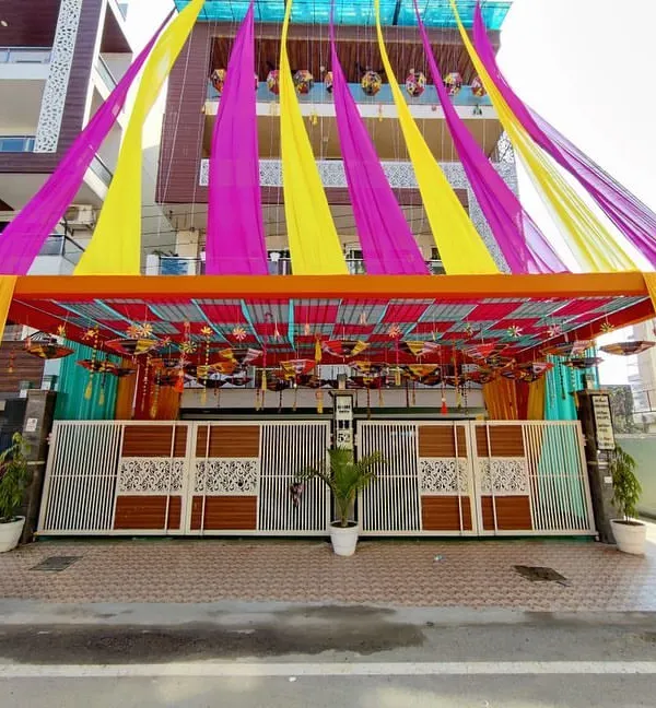 We build impressive entrance structures using pipe pandaals and decorate them with colorful drapes. This setup for a home ceremony uses bright yellow, pink, and orange fabrics for a grand welcome.