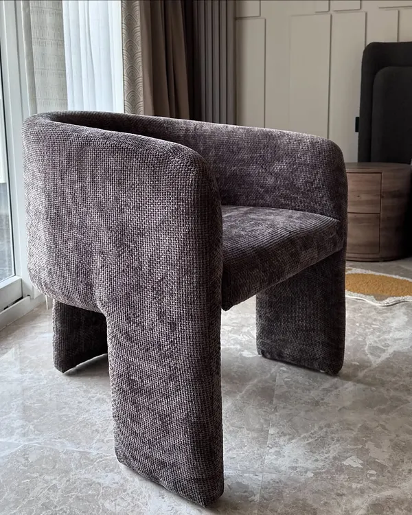 A modern accent chair upholstered in a rich, textured grey fabric. The chair's unique, sculptural form with its solid block legs makes it a statement piece in any room.