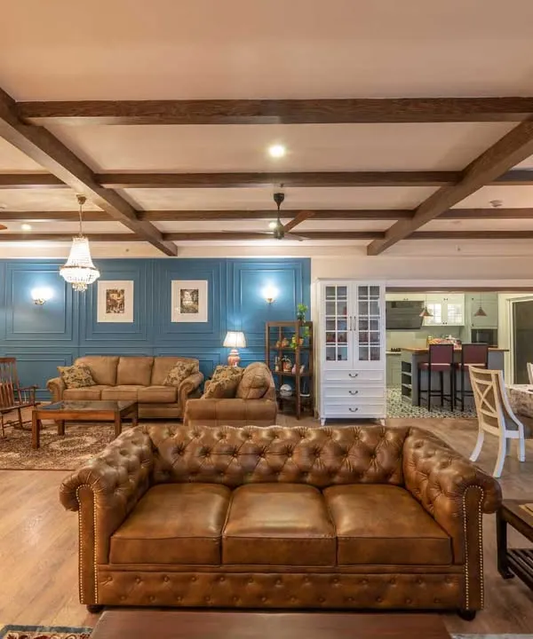 An expansive view of a home where industrial and Victorian styles merge. The open layout connects two distinct seating areas and a dining space, unified by wooden ceiling beams and a consistent color palette, making it ideal for large gatherings.