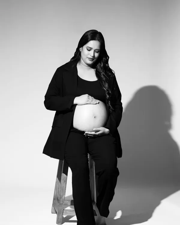 A quiet, contemplative moment captured in a black and white studio portrait. The mom-to-be is seated, gently holding her belly, creating a simple yet powerful image about the bond with her baby.