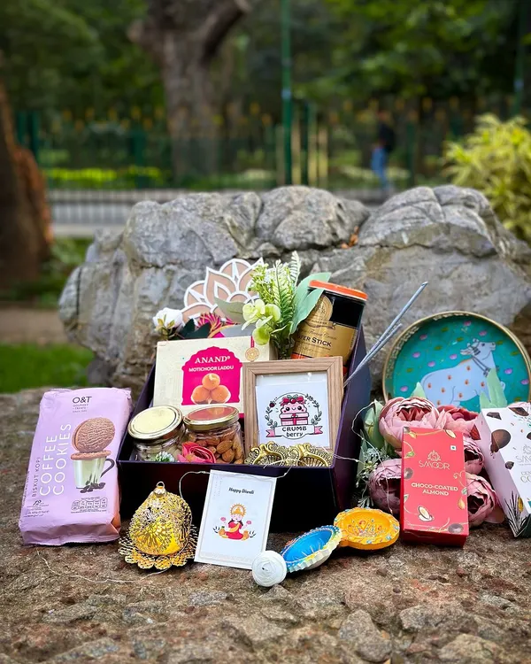 Our classic Diwali hamper, beautifully displayed outdoors. This gift box is filled with coffee cookies, jars of nuts, traditional Indian sweets, decorative diyas, and a personalized photo frame, making it a complete festive package.