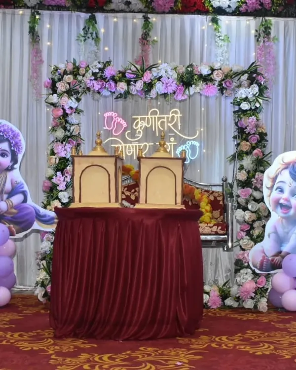 A complete Dohale Jevan stage setup featuring a floral arch, a 'Kunitari Yenar Ga' neon sign, and cute Krishna cutouts.