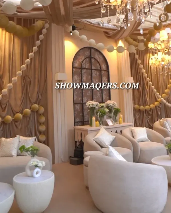 An elegant lounge area designed for a daytime event. The decor features plush ivory sofas, draped fabrics, and balloon garlands, creating a comfortable and luxurious space for guests to relax.